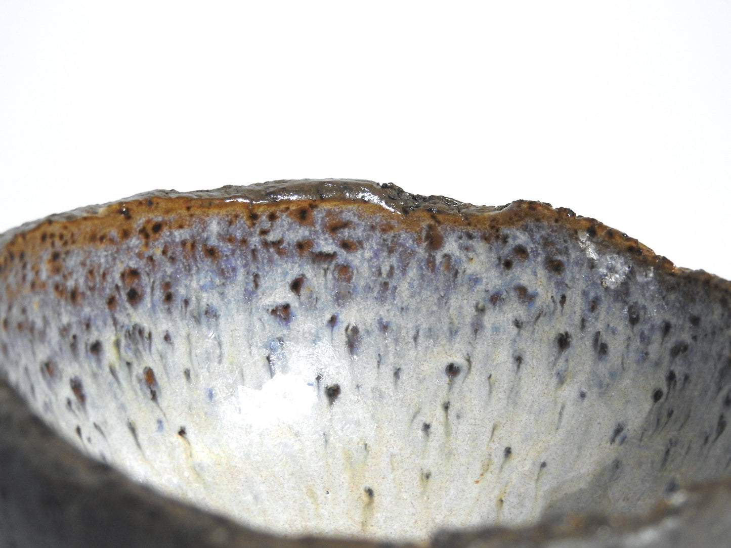 Close-up of the STONE DIP BOWL, a handmade piece with a rough, uneven rim. Its glaze blends brown, gray, and blue tones with speckled and streaked patterns, inspired by Greek pottery. Shown against a plain white background.