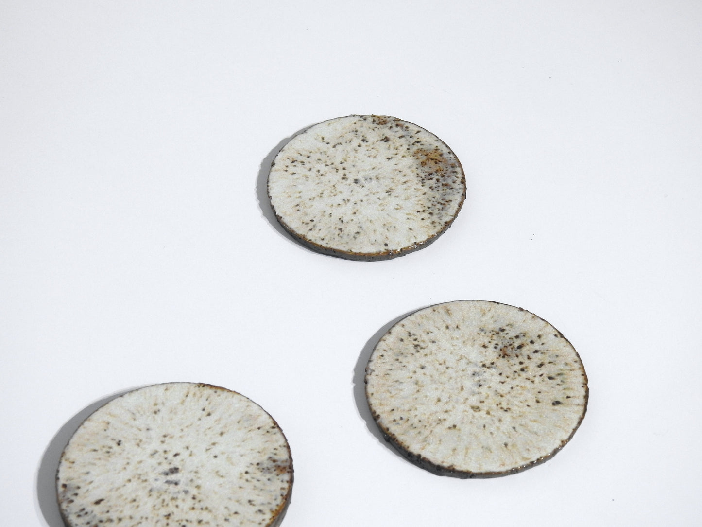Four round stone coasters from the STONE COASTERS SET OF 4, featuring a speckled light brown design and white marbled patterns, are arranged on a plain white background, creating a look of simple elegance.