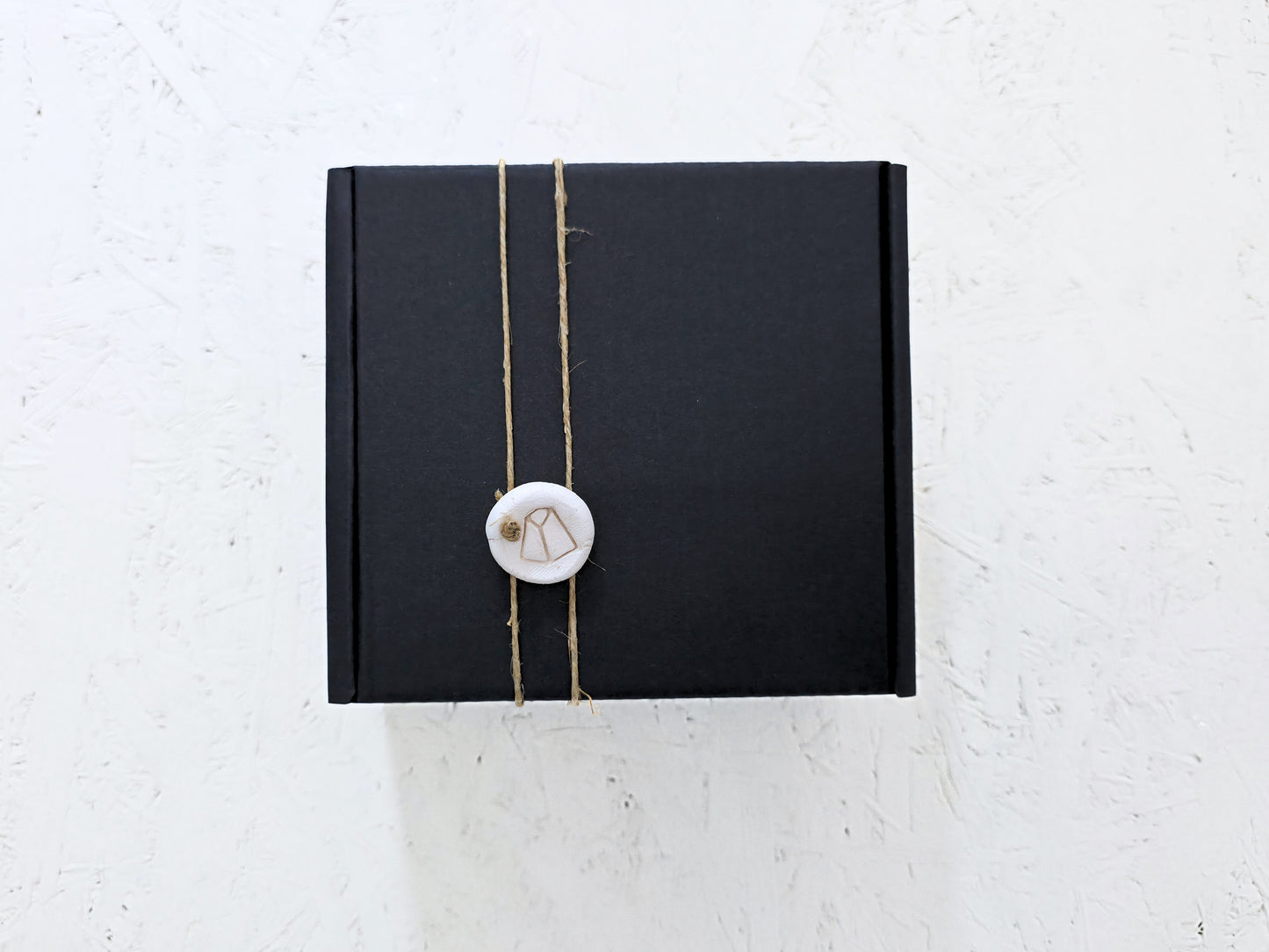 Box 10 by Magma Lab, a luxury gift box tied with twine and sealed with a round white wax stamp, is perfect for Christmas gifting and looks elegant on any textured white surface.