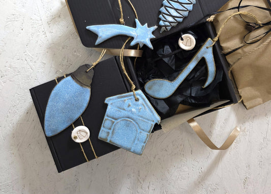 Box 3 is a luxury gift set featuring blue handcrafted ceramic Christmas ornaments—a light bulb, shooting star, house, and musical note—beautifully presented with gold ribbons and tissue paper for elegant gifting.