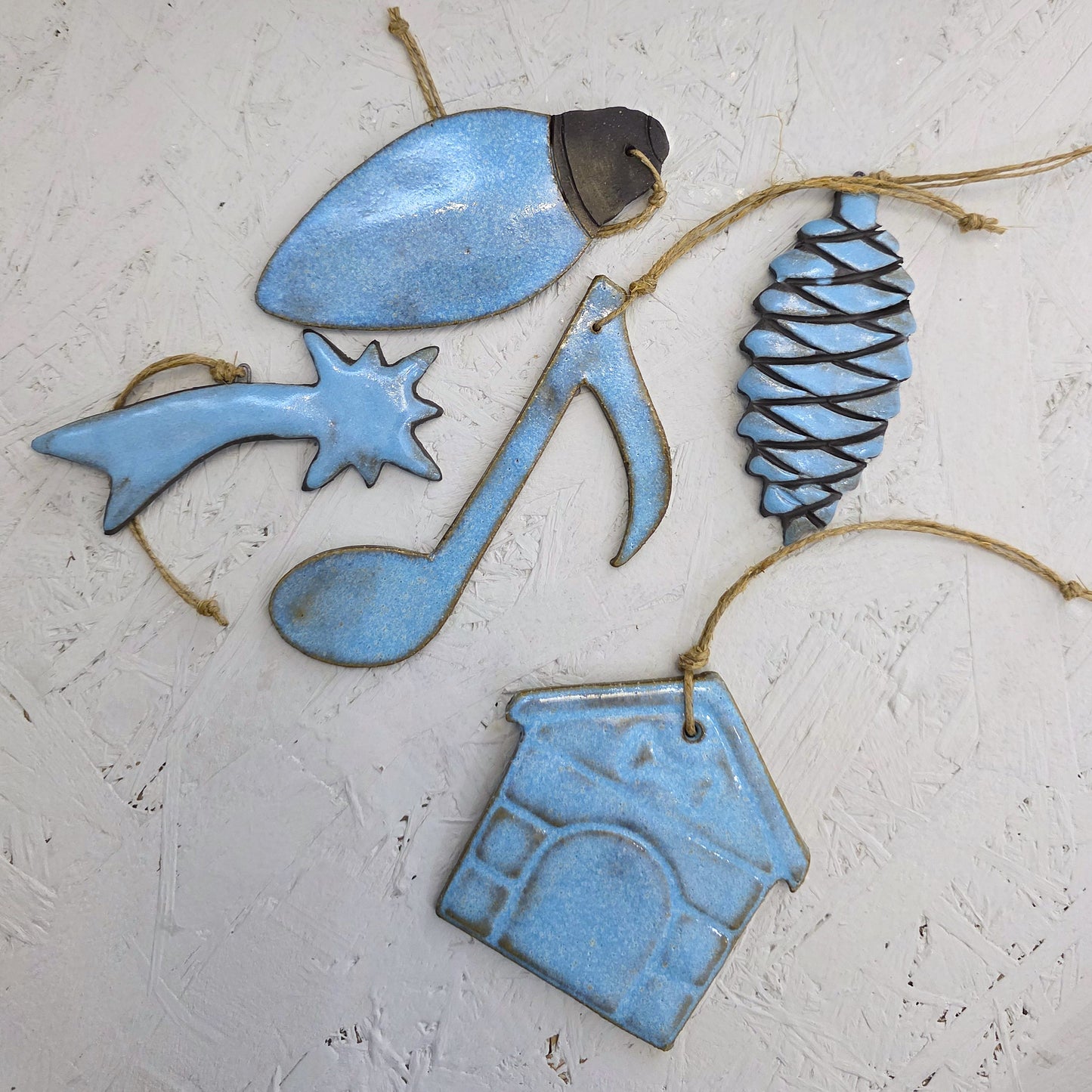 Box 3 features five handcrafted light blue ceramic ornaments (pinecone, music note, house, star with a trail, light bulb) with twine loops on a white textured surface—ideal for Christmas gifts.