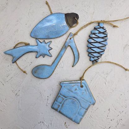 Box 3 features five handcrafted light blue ceramic ornaments (pinecone, music note, house, star with a trail, light bulb) with twine loops on a white textured surface—ideal for Christmas gifts.