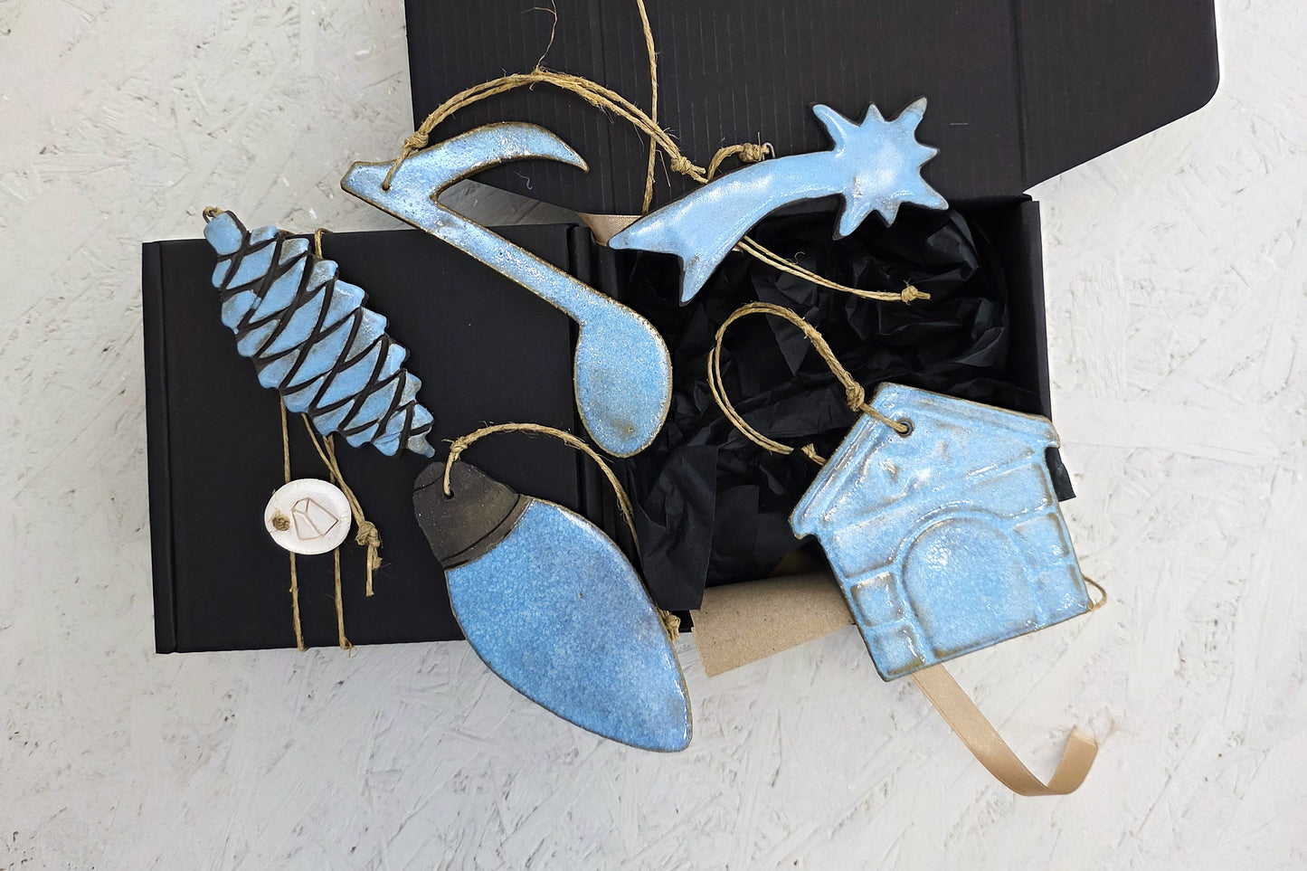 Box 3 features a luxury gift box with black tissue paper containing handcrafted ceramic ornaments—a blue pine cone, musical note, shooting star, Christmas light bulb, and house—each with twine for hanging. Perfect for Christmas gifting.