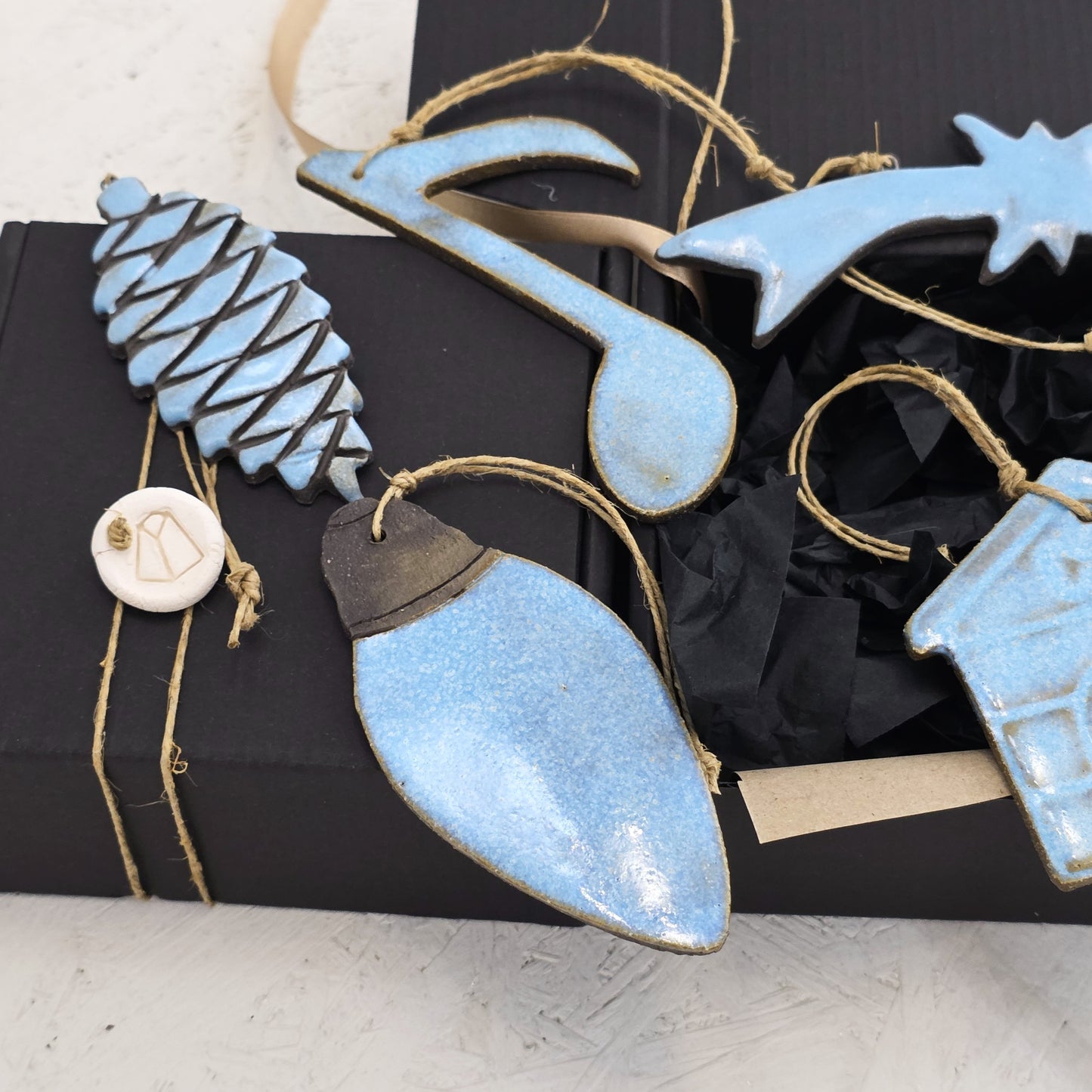 Box 3 features handcrafted ceramic ornaments—pinecone, musical note, star, lightbulb, and house—each glazed in light blue and presented on a black luxury gift box with twine. An elegant choice for Christmas gifting.
