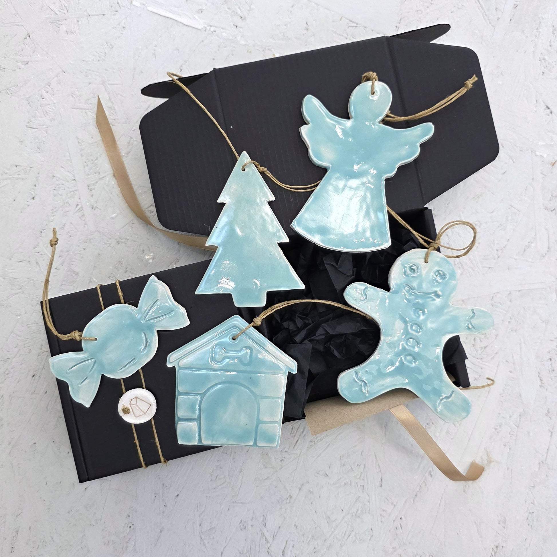 Box 4 features five glossy, handcrafted light blue ceramic ornaments—a candy, house, tree, angel, and gingerbread person—arranged with a luxury gift box tied in brown ribbon. A beautiful choice for Christmas gifting.