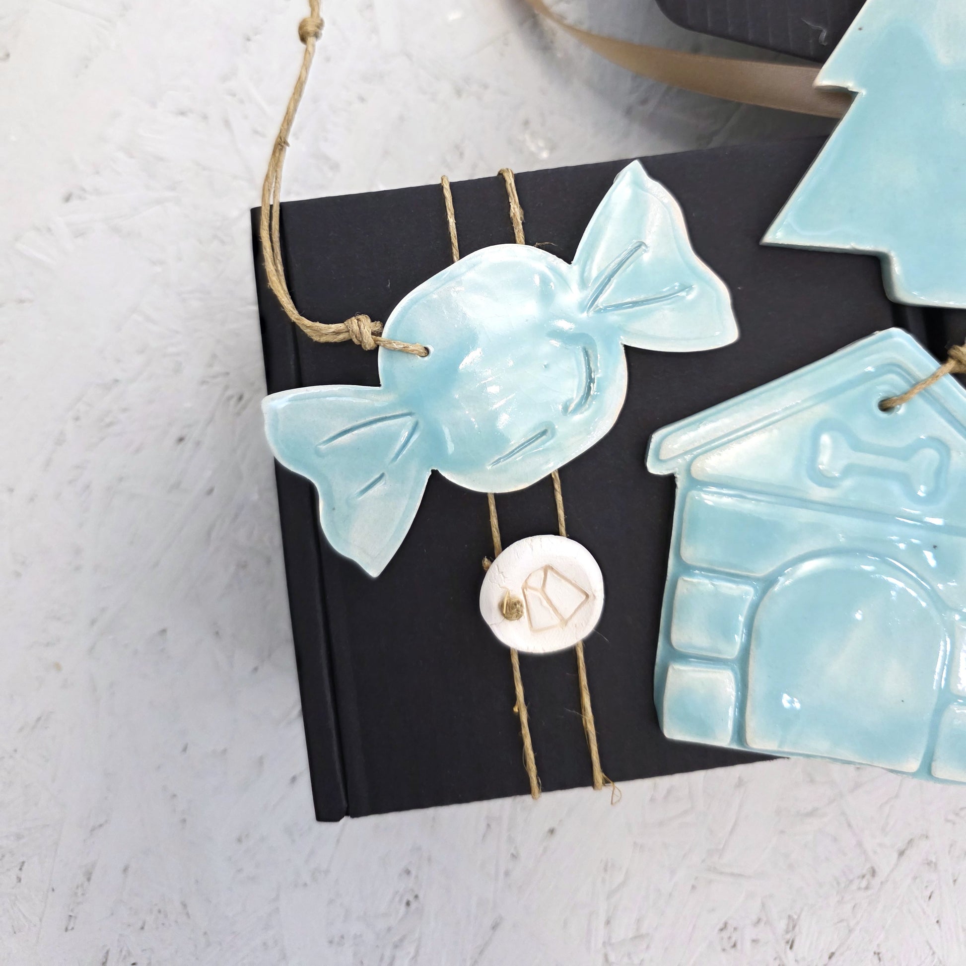 Box 4 features a pale blue, handcrafted ceramic candy-shaped ornament and a house-shaped ornament, displayed on a luxury gift box with twine. Set against a light textured background, it’s ideal for Christmas gifting.