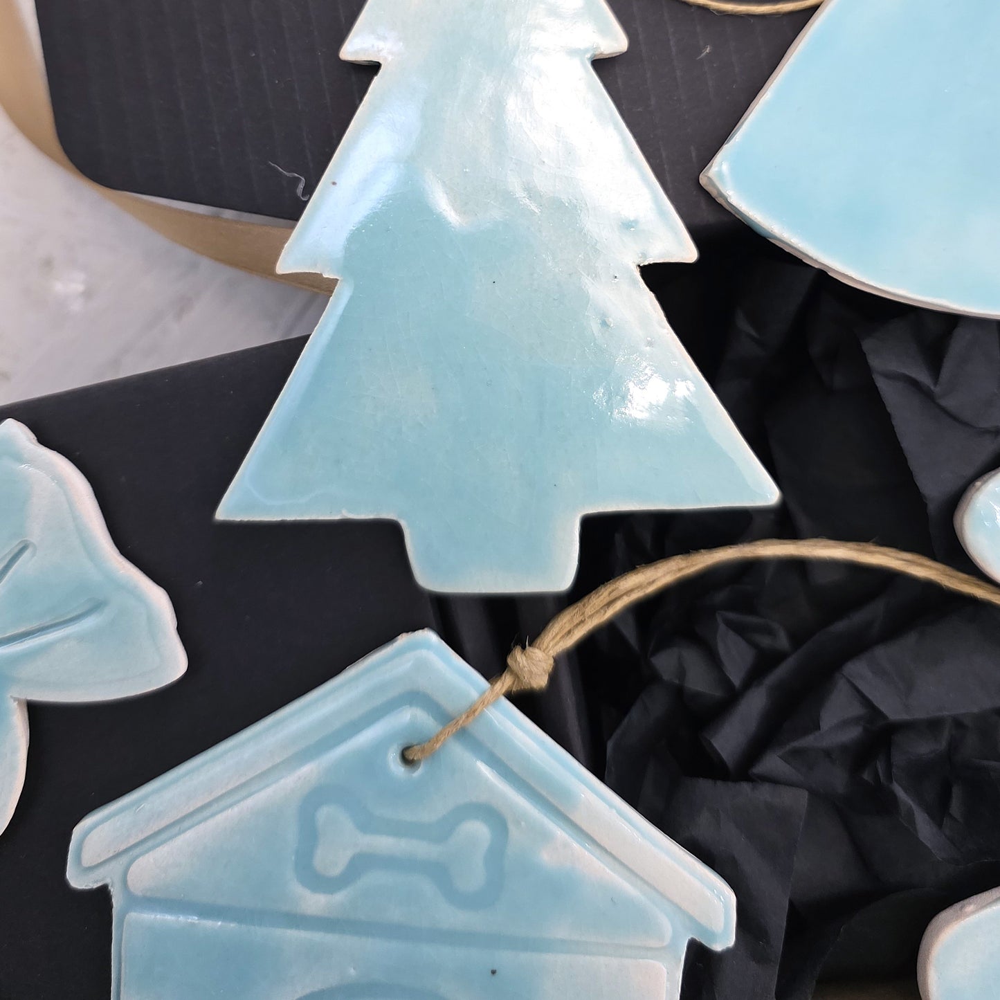 Box 4 features light blue handcrafted ceramic ornaments—a Christmas tree, house with bone symbol, and bell—each with twine for hanging. Presented on black crinkled paper, they’re perfect for Christmas gifting or luxury gift boxes.
