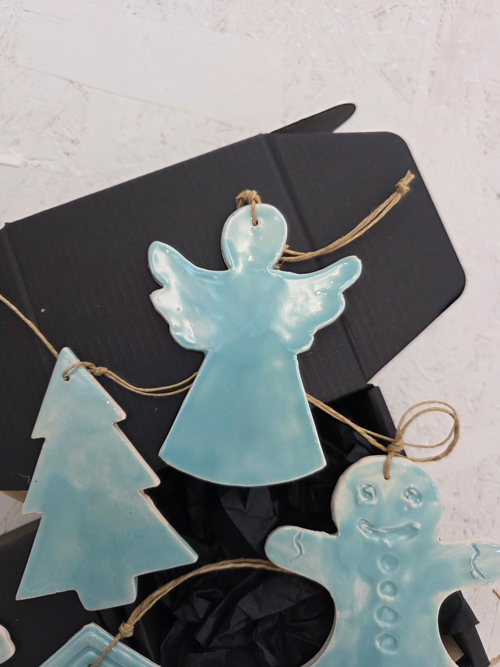 Box 4 features handcrafted pale blue ceramic ornaments—angel, Christmas tree, and gingerbread person—tied with string and beautifully presented on black tissue in a luxury gift box, perfect for thoughtful Christmas gifting.