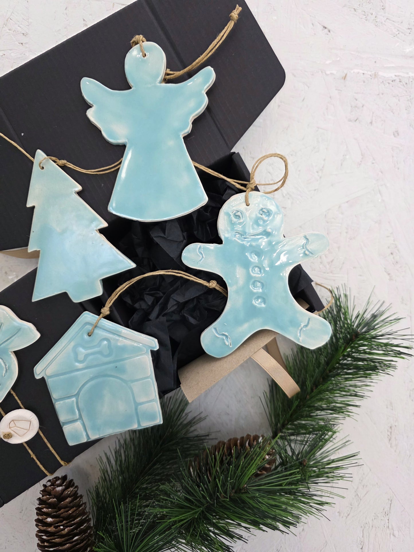 Box 4 is a luxury gift box with handcrafted light blue ceramic ornaments—angel, tree, gingerbread person, and house—nestled among pine branches and pinecones. It’s the perfect elegant Christmas gift.