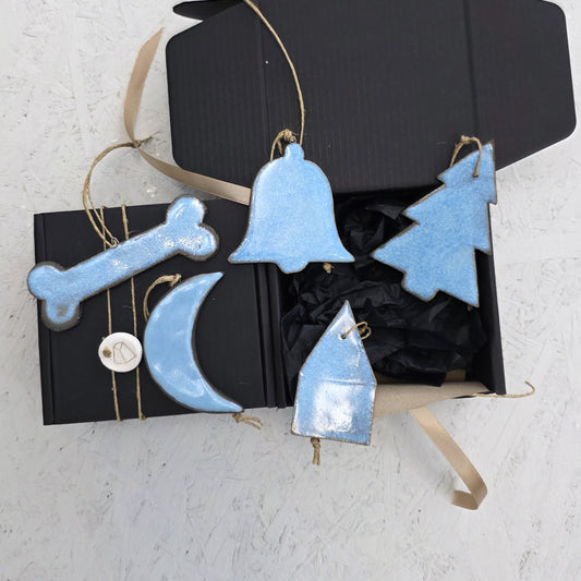 Box 5 is a luxury gift box with a ribbon, featuring handcrafted blue ceramic ornaments—bell, tree, house, moon, and bone with twine loops—displayed on a white textured surface. Perfect for Christmas gifting.