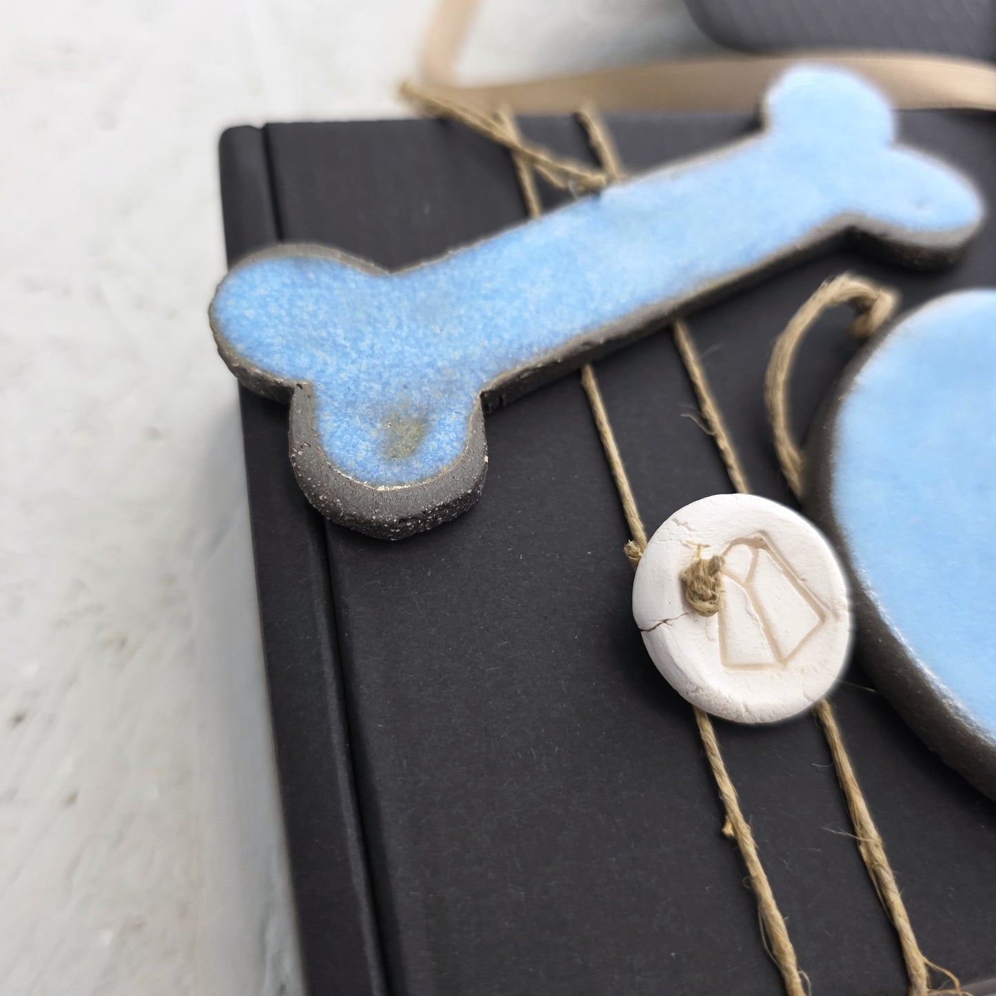 A close-up of Box 5, a luxury gift box adorned with handcrafted blue ceramic bone, blue oval, and small white round charm tied with twine—perfect for Christmas gifting.