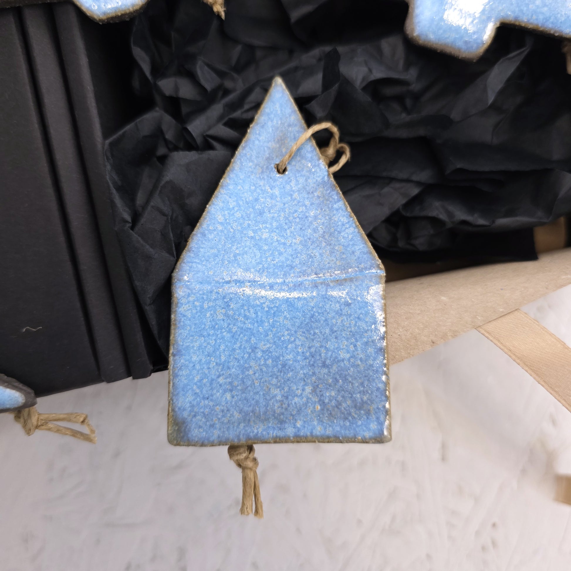 Box 5 is a blue handcrafted ceramic house ornament with a pointed roof and twine loop, displayed on crumpled black paper—an ideal Christmas gift.