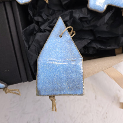 Box 5 is a blue handcrafted ceramic house ornament with a pointed roof and twine loop, displayed on crumpled black paper—an ideal Christmas gift.