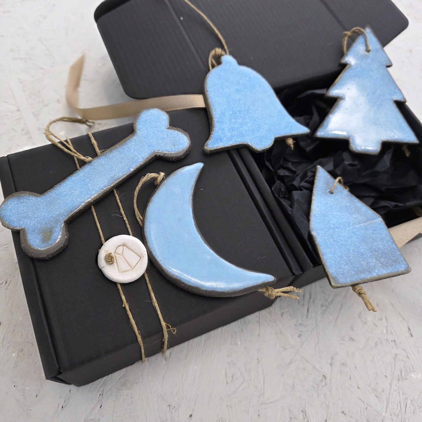 Box 5 features five handcrafted light blue ceramic ornaments—a bone, bell, tree, moon, and house—displayed with two black luxury gift boxes tied with string, making it perfect for thoughtful Christmas gifting.