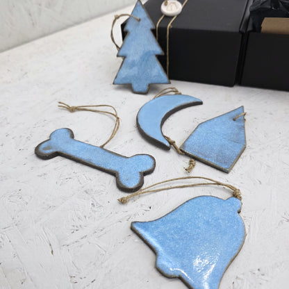 Box 5 includes five blue handcrafted ceramic ornaments—tree, moon, house, bone, and bell shapes—each with twine loops. Displayed on a textured white surface with a luxury gift box, they’re perfect for Christmas gifting.