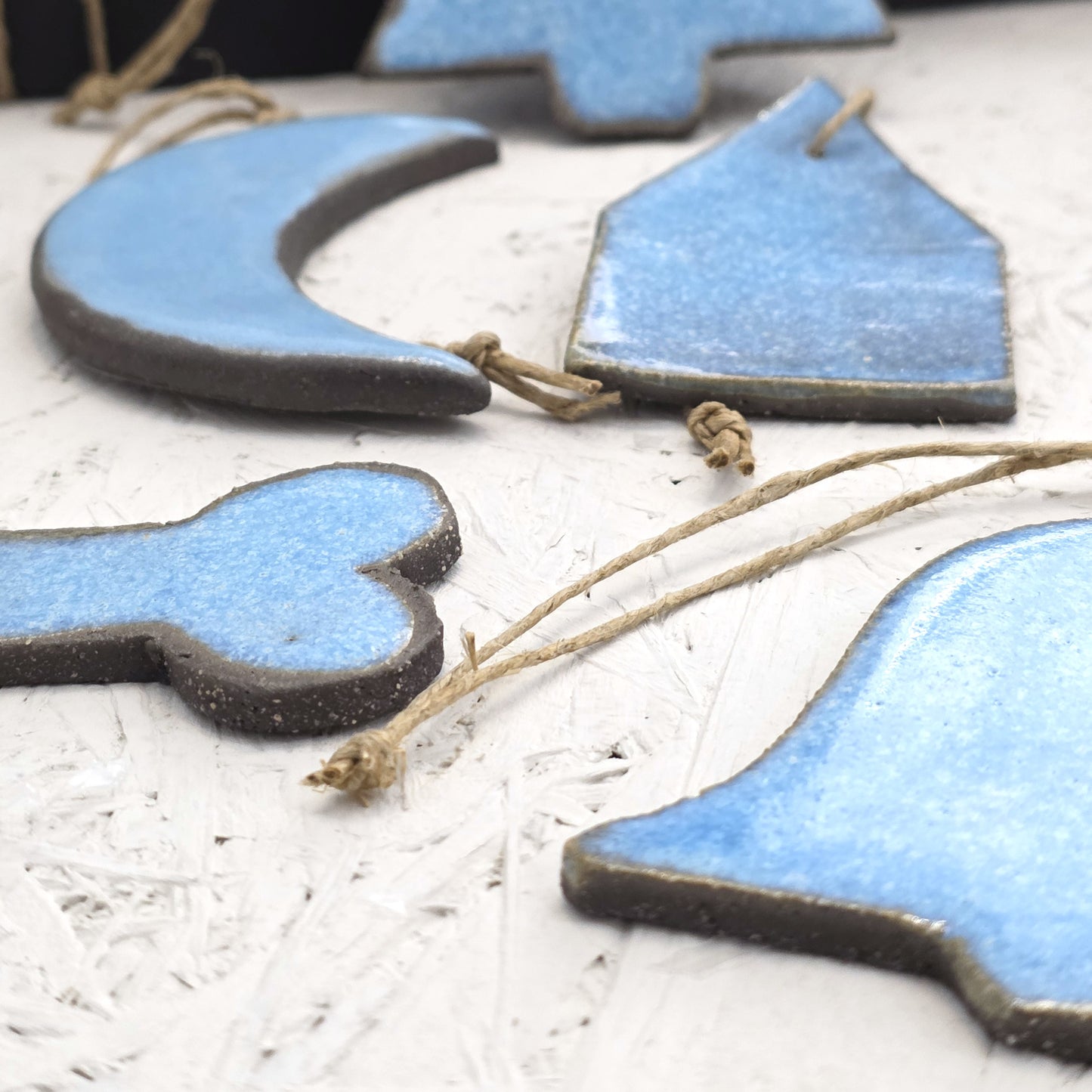 Close-up of Box 5: handcrafted ceramic ornaments—moon, house, bone, and bell shapes—each with a twine loop for hanging, arranged on textured white. Ideal for Christmas gifts or adding to a luxury gift box.