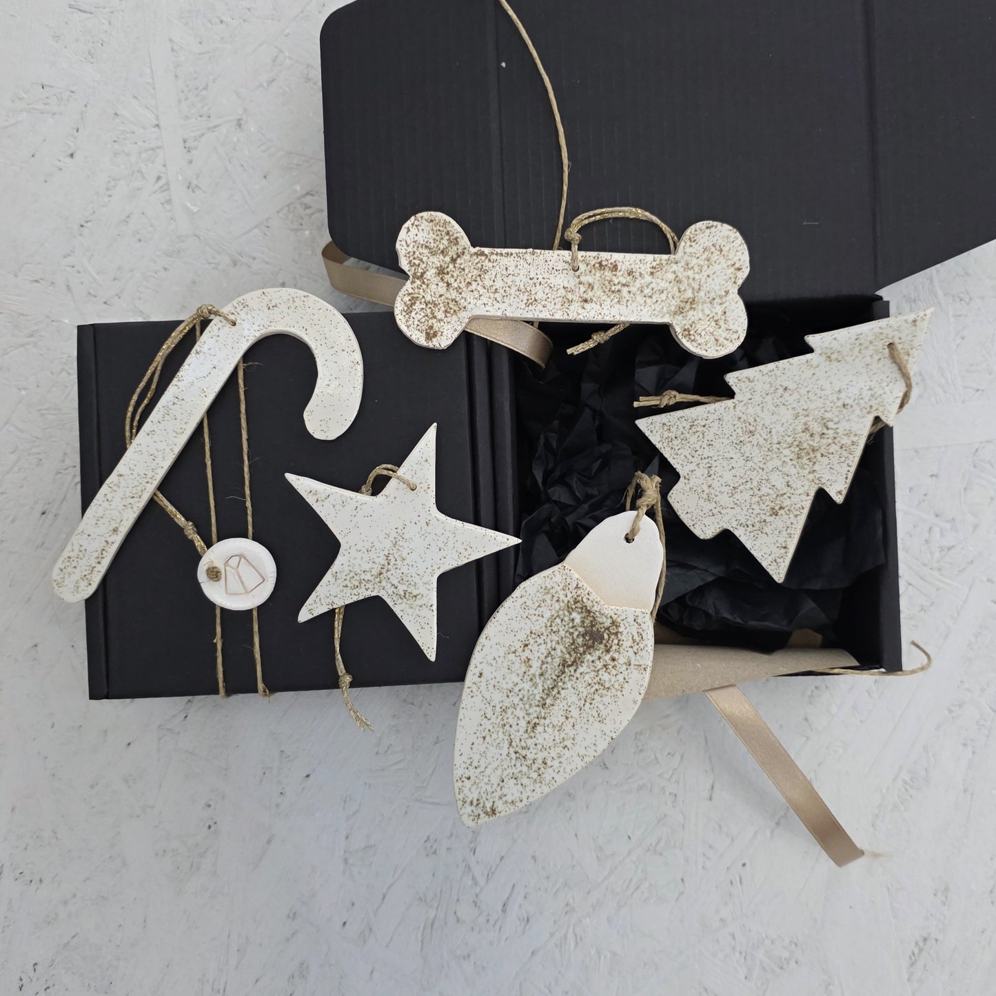 Box 7 is a black handcrafted gift box with festive white luxury ceramic ornaments—candy cane, star, tree, bone, and leaf—sprinkled with gold glitter and tied with twine. The box sits partially open on a light textured surface.
