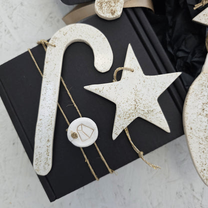 Box 7 is a handcrafted black gift box, decorated with rustic ornaments including a luxury ceramic candy cane, star, and a round tag with geometric line art—all tied with twine for an elegant Christmas gift.