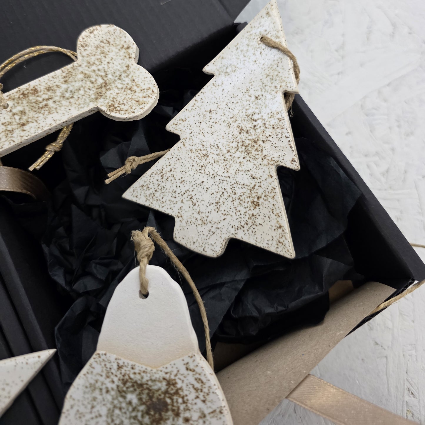Box 7 is a black gift box with handcrafted ceramic Christmas ornaments—a tree, bone, and penguin—each brown-speckled and hung on twine. Lined with black tissue paper, it’s ideal for Christmas gifting.