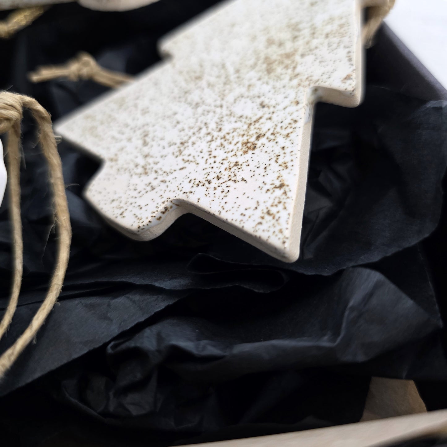 A close-up of Box 7, a luxury white ceramic tree ornament with gold speckles, lying on crumpled black tissue paper—perfect for Christmas gifting and ready to hang.