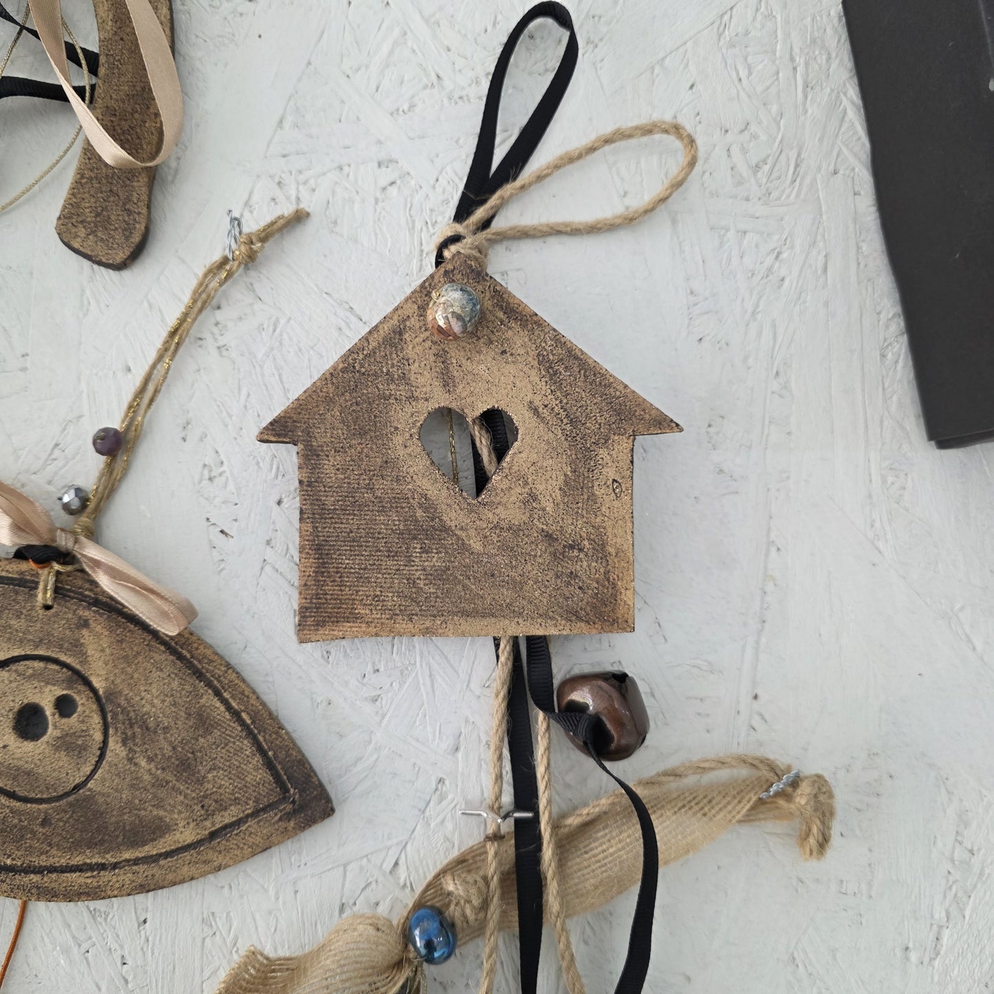 The Lucky charm House is a handcrafted rustic house-shaped ornament with a heart cutout, black ribbon, twine, beads, and a bell—perfect for festive traditions and pairing with handmade ceramic Christmas charms.