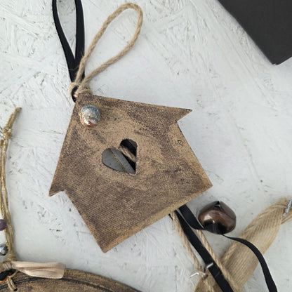 The Lucky Charm House is a small wooden house-shaped ornament with a heart cutout, twine, beads, and a black ribbon—perfect for festive traditions and pairing with handmade ceramic Christmas charms.