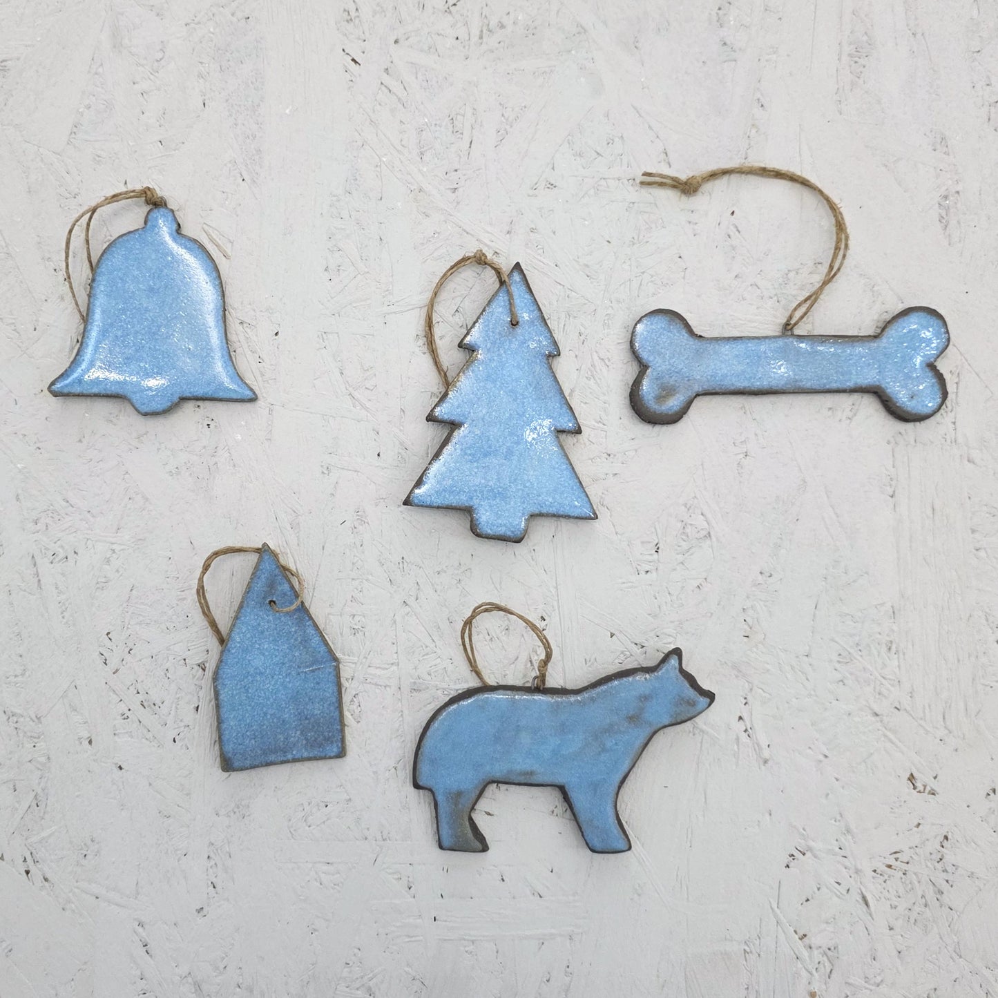 Five handcrafted blue ceramic ornaments from Magma Lab’s Box 8—featuring a bell, tree, bone, house, and bear with twine loops—make a perfect luxury holiday gift or limited edition keepsake.