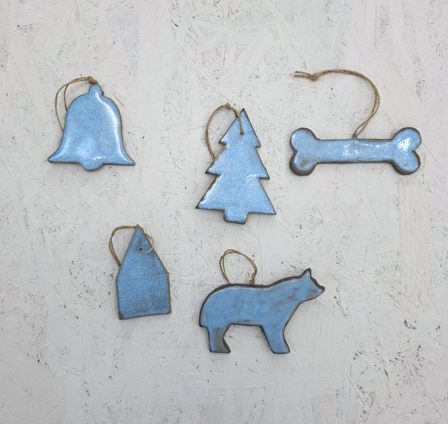 The Magma Lab Box 8 features five blue luxury ceramic ornaments—bell, tree, bone, house, and bear—with twine loops, beautifully arranged on a light textured surface and presented in a handcrafted gift box. Limited edition.