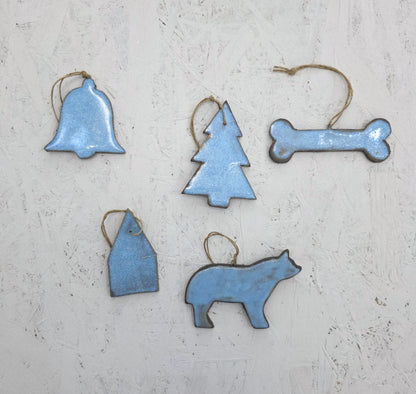 The Magma Lab Box 8 features five blue luxury ceramic ornaments—bell, tree, bone, house, and bear—with twine loops, beautifully arranged on a light textured surface and presented in a handcrafted gift box. Limited edition.