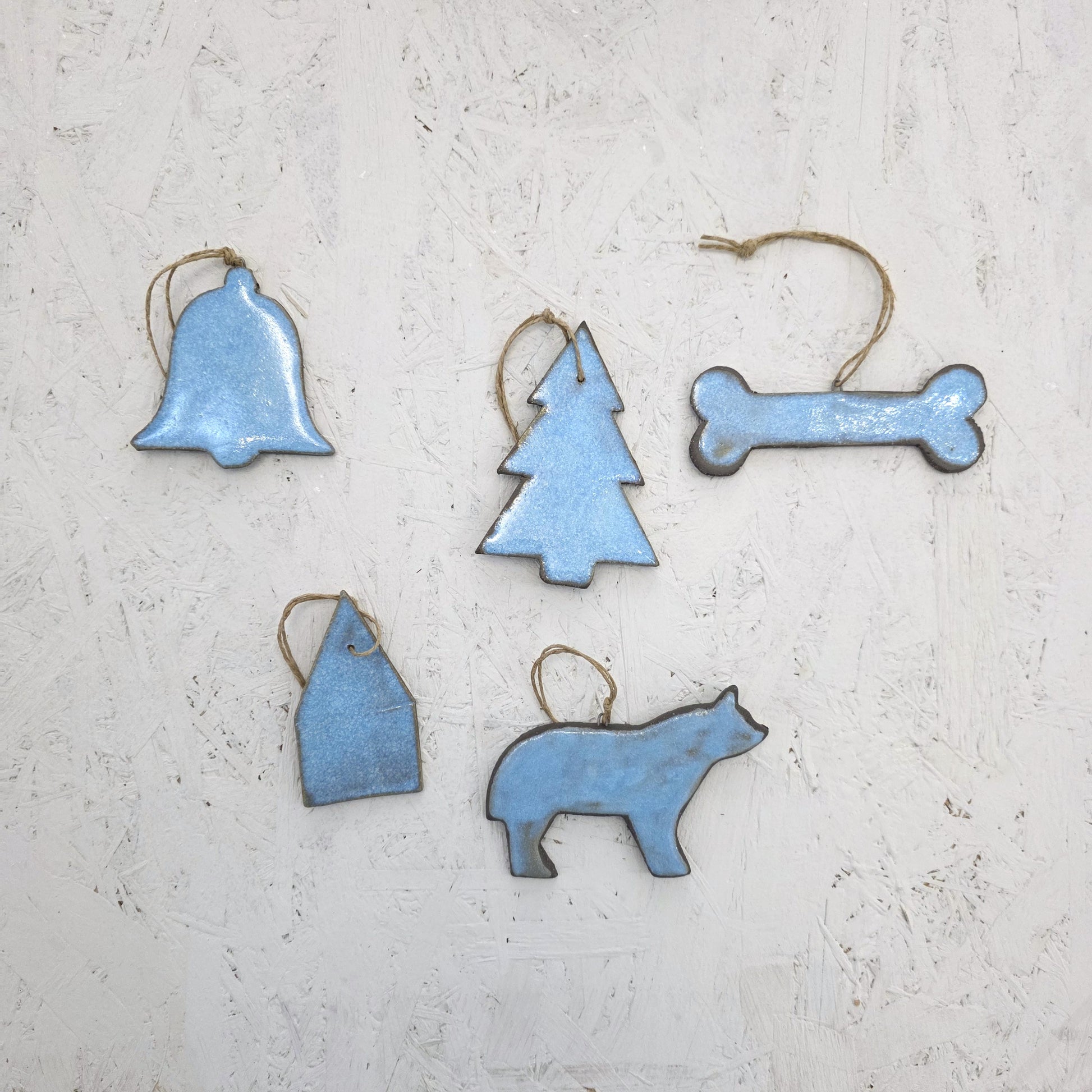 Box 8 by Magma Lab features five blue luxury ceramic ornaments—bell, Christmas tree, bone, house, and animal shapes—with twine loops against a white background. A perfect limited edition handcrafted gift box.