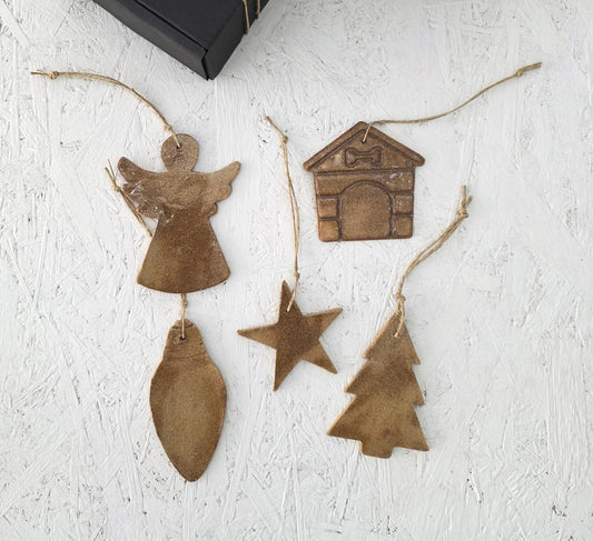 Five handcrafted brown ceramic ornaments—angel, house, star, tree, and teardrop—by Magma Lab hang on twine. Presented with a sleek black Box 10 gift box, they're perfect for Christmas gifting.