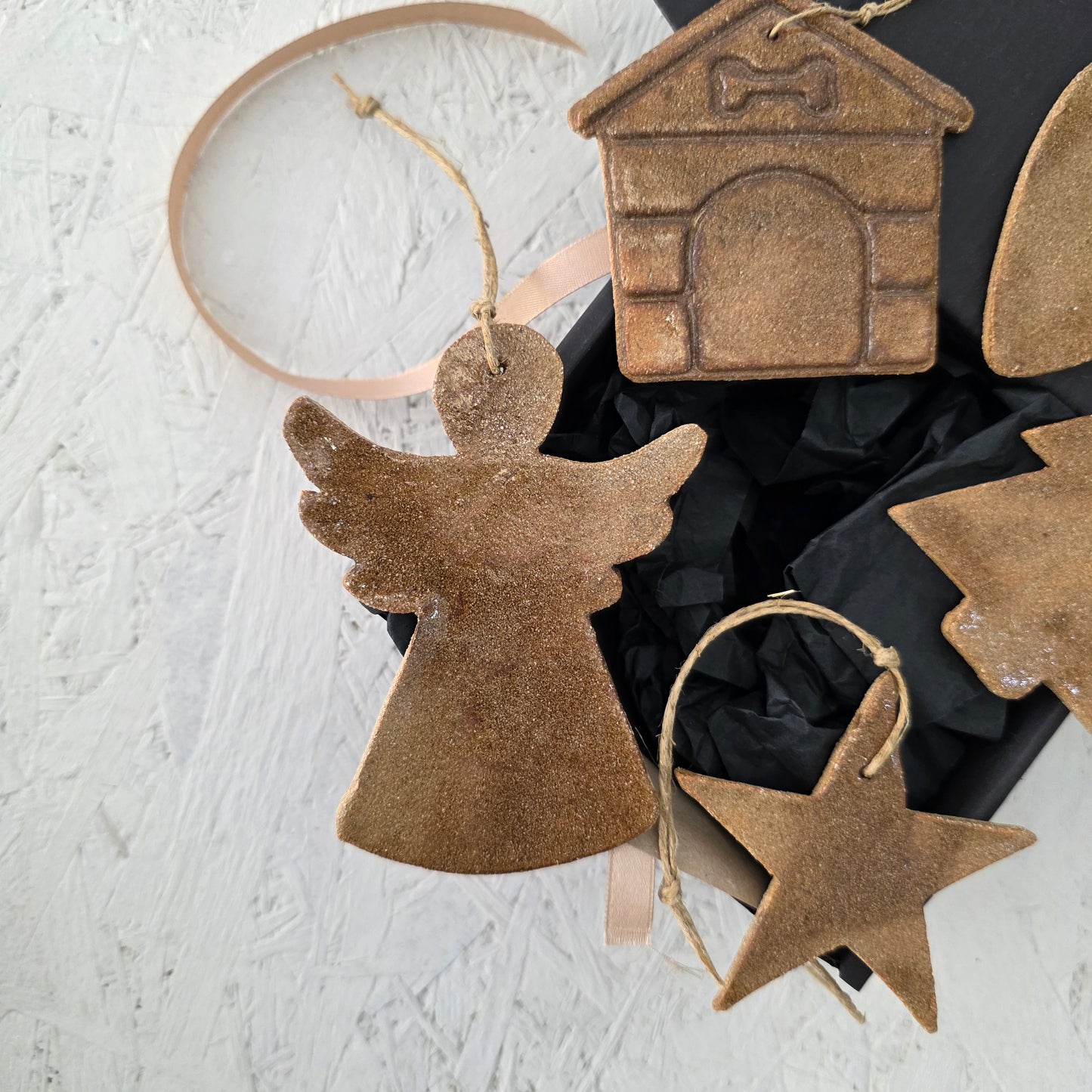 Box 10 by Magma Lab features four handcrafted ceramic ornaments—angel, star, tree, and house—with string loops, displayed on a white textured surface and elegantly packaged in a luxury gift box for thoughtful Christmas gifting.