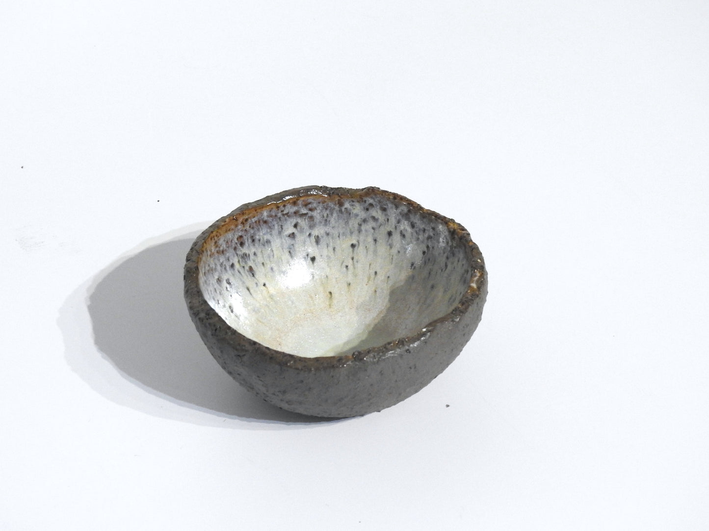 The STONE DIP BOWL is a small, round stoneware bowl with a rough, dark exterior and a smooth, speckled light interior. It is shown on a plain white background.