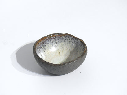 The STONE DIP BOWL is a small, round stoneware bowl with a rough, dark exterior and a smooth, speckled light interior. It is shown on a plain white background.