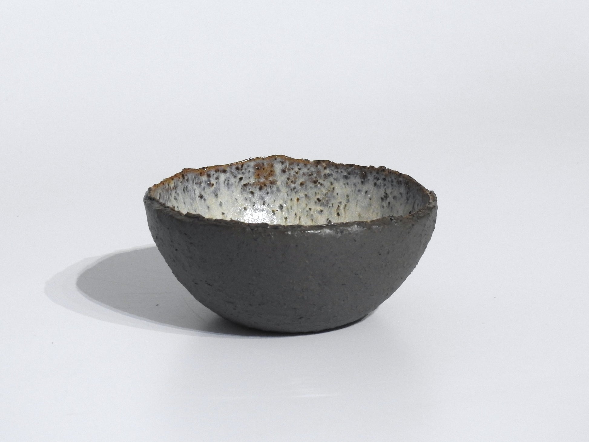 The STONE STARTER BOWL is a handmade serving bowl inspired by Greek pottery, with a rough dark gray exterior and a speckled white interior, shown on a plain white background.