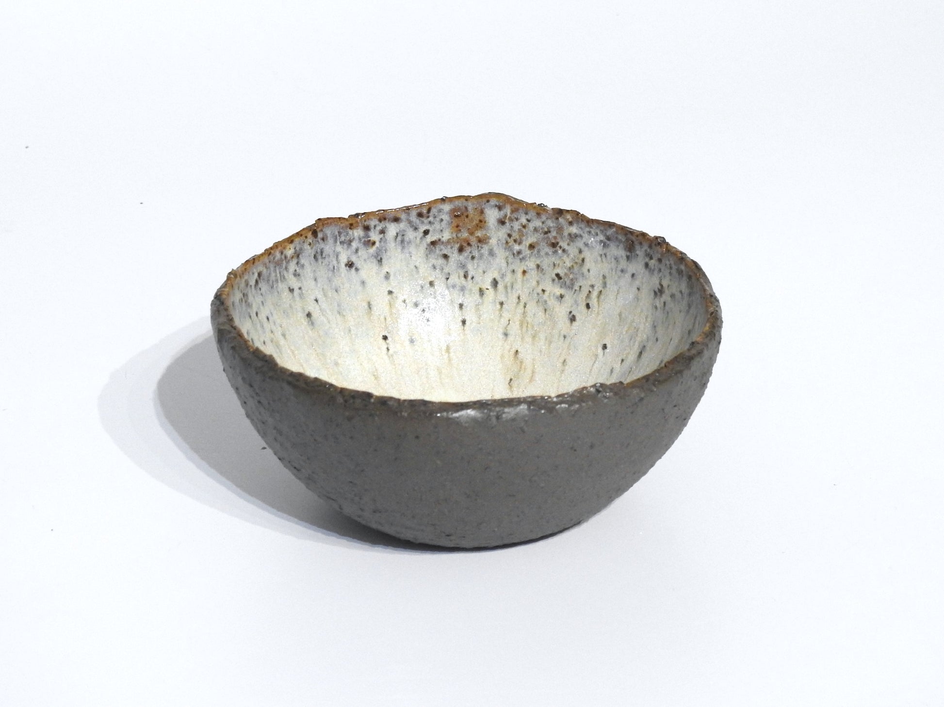 The STONE STARTER BOWL is a handmade serving bowl inspired by Greek pottery, featuring a rough, grey stoneware-like exterior and a smooth, speckled white interior, displayed on a plain white background.