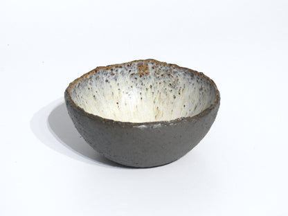 The STONE STARTER BOWL is a handmade serving bowl inspired by Greek pottery, featuring a rough, grey stoneware-like exterior and a smooth, speckled white interior, displayed on a plain white background.