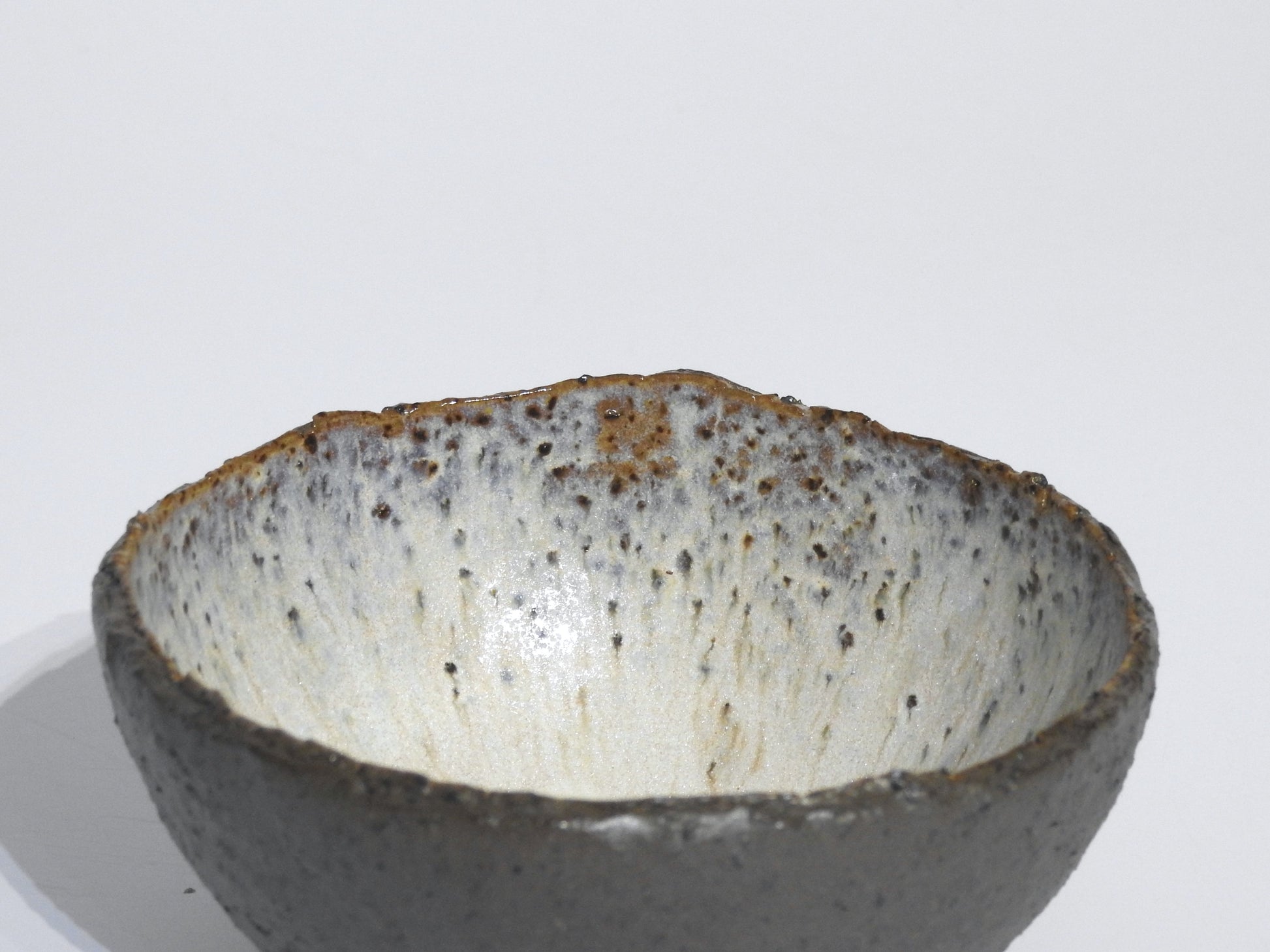 The STONE STARTER BOWL is a handmade grey stoneware serving bowl inspired by Greek pottery, featuring a rough uneven rim and a speckled white and brown glaze interior, shown against a plain white background.