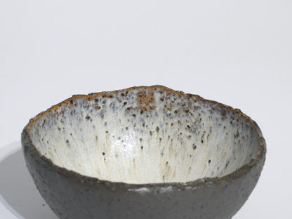 The STONE STARTER BOWL is a handmade grey stoneware serving bowl inspired by Greek pottery, featuring a rough uneven rim and a speckled white and brown glaze interior, shown against a plain white background.