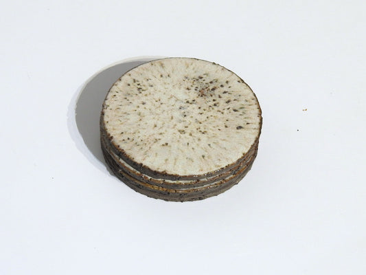 The STONE COASTERS SET OF 4 features round, flat white coasters with speckled brown spots and textured edges, resembling handmade stoneware, shown stacked on a white background.
