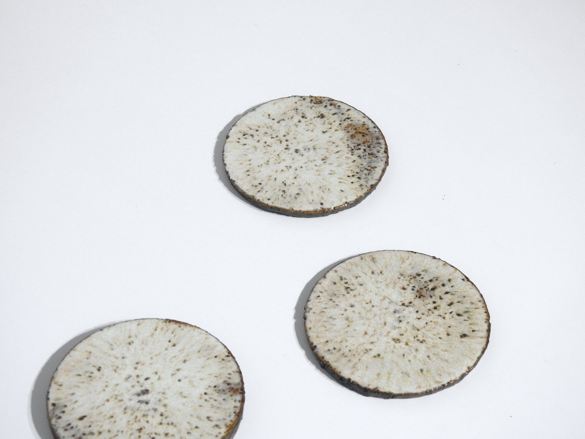 Four round stone coasters from the STONE COASTERS SET OF 4, featuring a speckled light brown design and white marbled patterns, are arranged on a plain white background, creating a look of simple elegance.