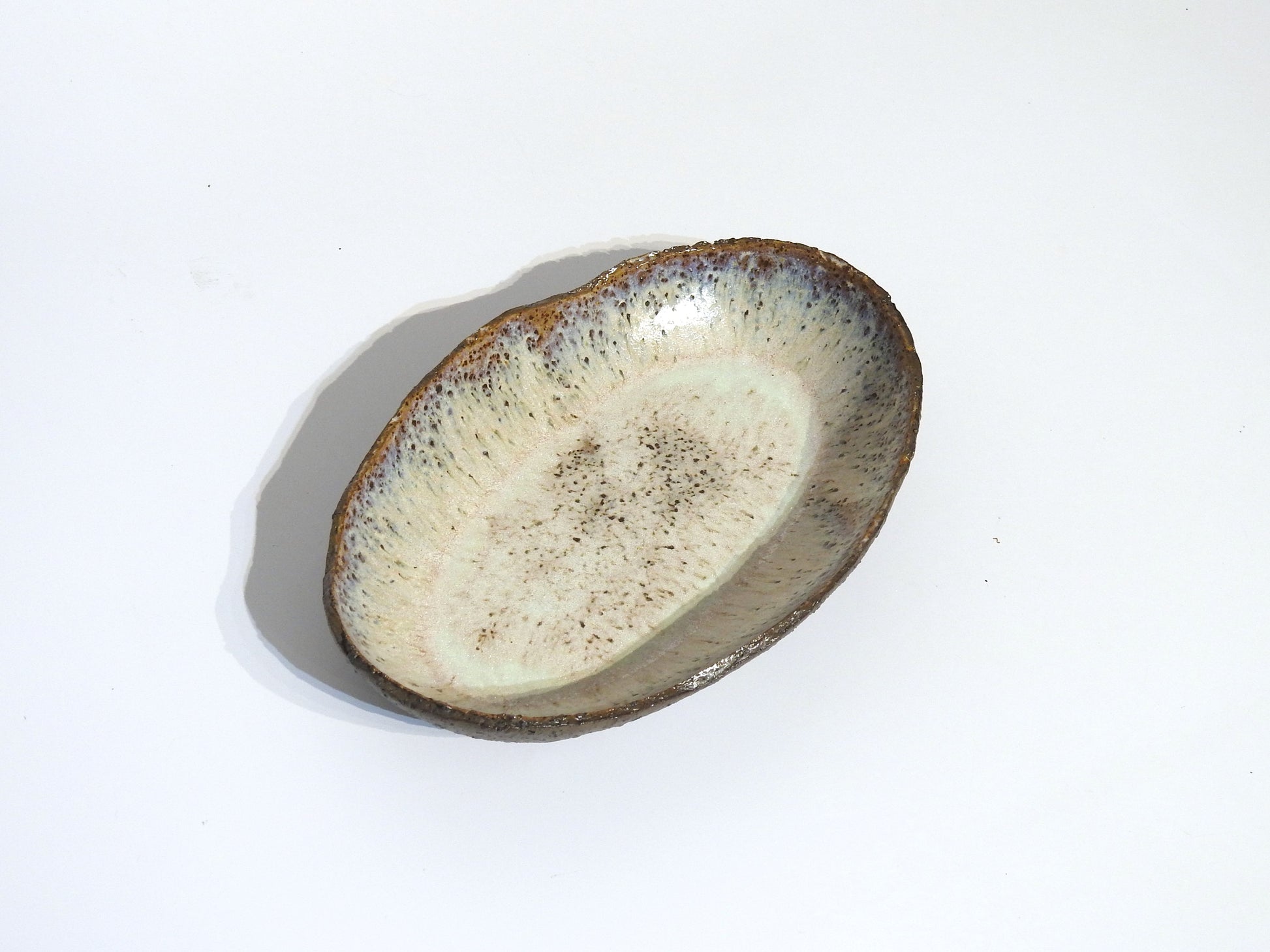 The STONE OVAL BOWL is a handmade ceramic dish featuring a textured, speckled glaze in earthy brown and cream tones. Measuring 24.5 cm long by 15.5 cm wide, it is displayed against a plain white background.