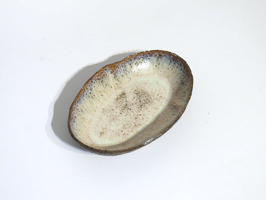 The STONE OVAL BOWL is a handmade ceramic dish featuring a textured, speckled glaze in earthy brown and cream tones. Measuring 24.5 cm long by 15.5 cm wide, it is displayed against a plain white background.