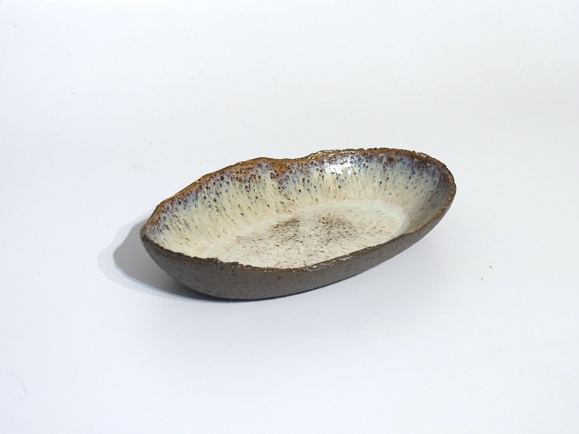 The STONE OVAL BOWL is handmade with a textured, earthy brown exterior and a lightly speckled off-white interior. It measures 24.5 cm long by 15.5 cm wide and is shown on a plain white background.