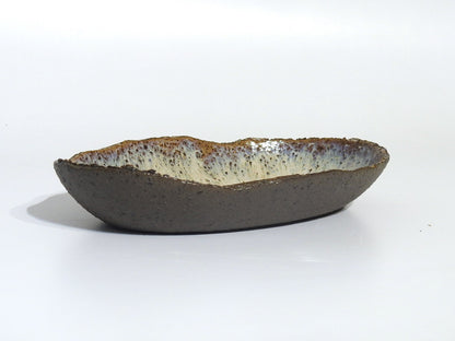 The STONE OVAL BOWL is handmade ceramic, featuring a rough dark brown exterior and speckled white and brown glazed interior. Measures 15.5 cm x 24.5 cm and is shown against a plain white background.