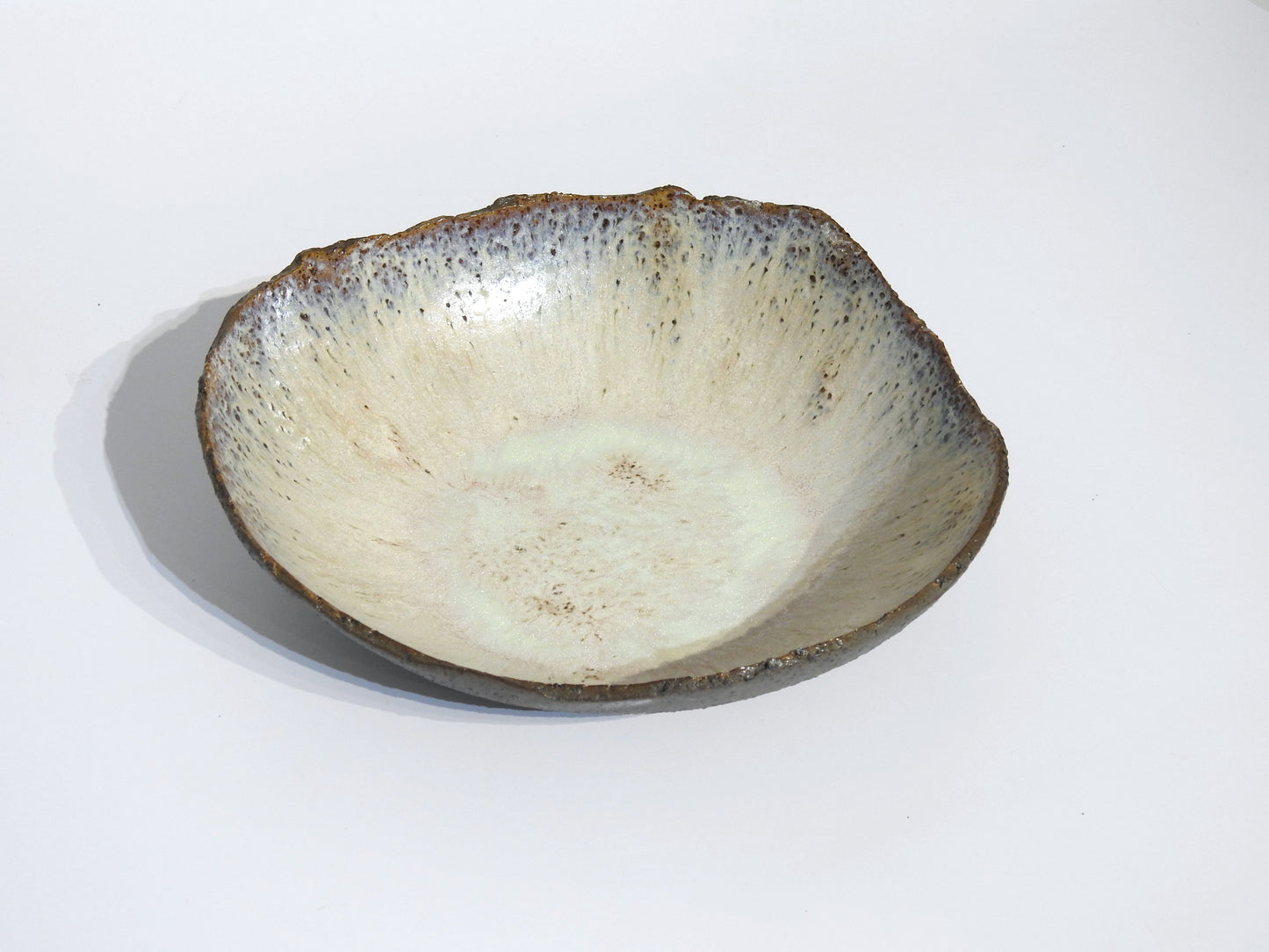 The STONE BIG SALAD BOWL is a handmade ceramic piece with a rough, uneven rim and speckled off-white glaze. Its organic, rustic look is highlighted by dimensions of 7.5 cm height and 25.5 cm width, shown on a plain white background.