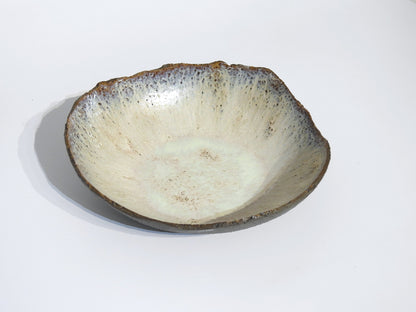 The STONE BIG SALAD BOWL is a handmade ceramic piece with a rough, uneven rim and speckled off-white glaze. Its organic, rustic look is highlighted by dimensions of 7.5 cm height and 25.5 cm width, shown on a plain white background.