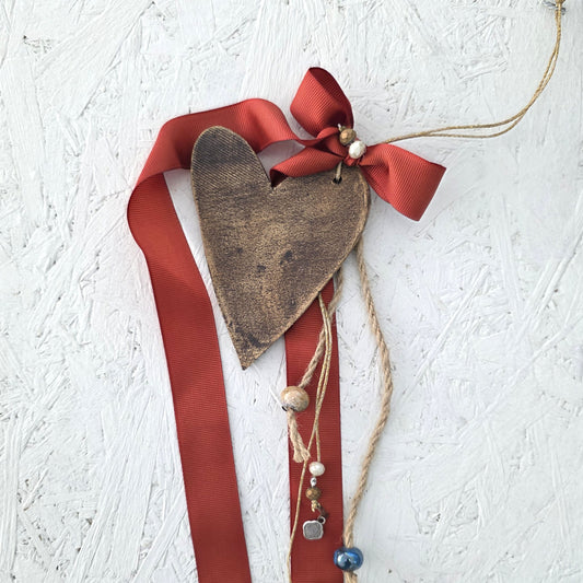 Decorative heart ornament with red ribbon and beads on a textured white background