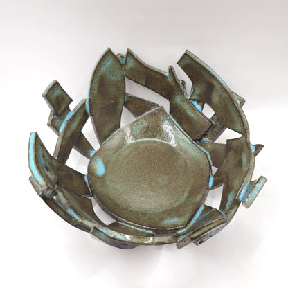 The ATLANTIS 'BRUTE' BOWL is a handmade stoneware piece with an abstract, irregular form, jagged overlapping edges, a smooth center, and a metallic iridescent glaze over black clay for a bold, modern look.