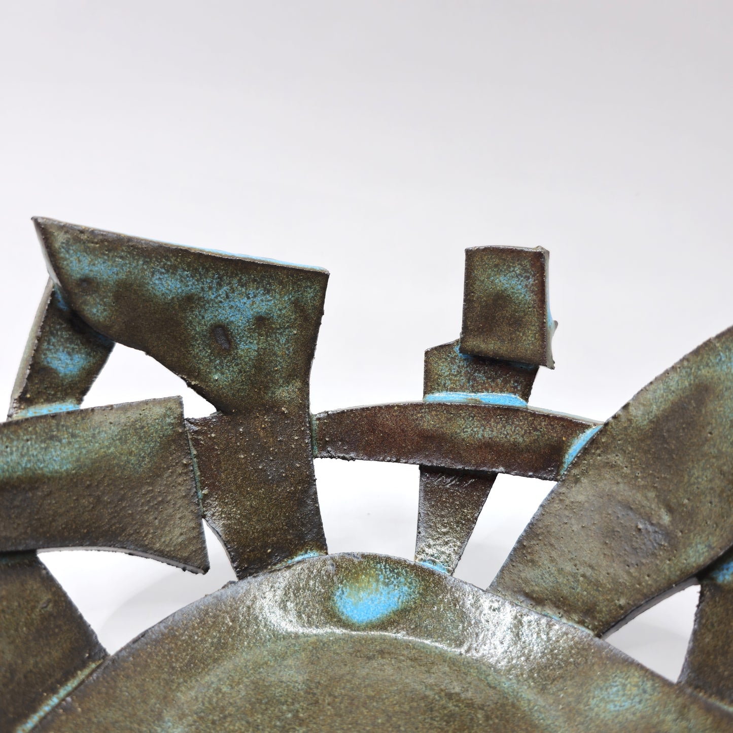 A close-up of the ATLANTIS 'BRUTE' BOWL, an abstract, handmade stoneware piece with geometric forms and a bronze-green patina, displayed against a plain white background.